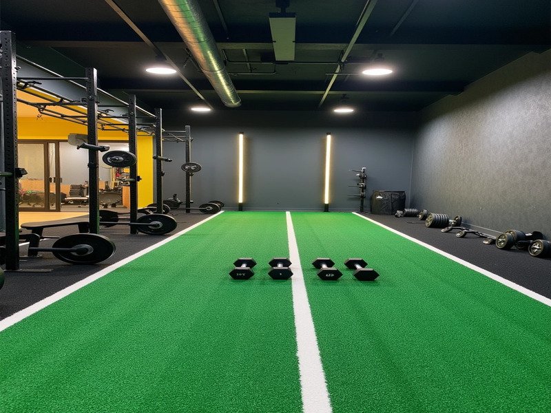 Una imagen dividida que muestra un trineo Hyrox sobre césped especializado y una clase en grupo sobre el césped general del gimnasio.